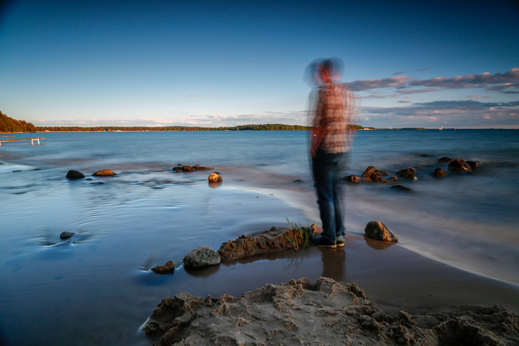 Människa som står och blickar ut över havet på låga havsklippor.