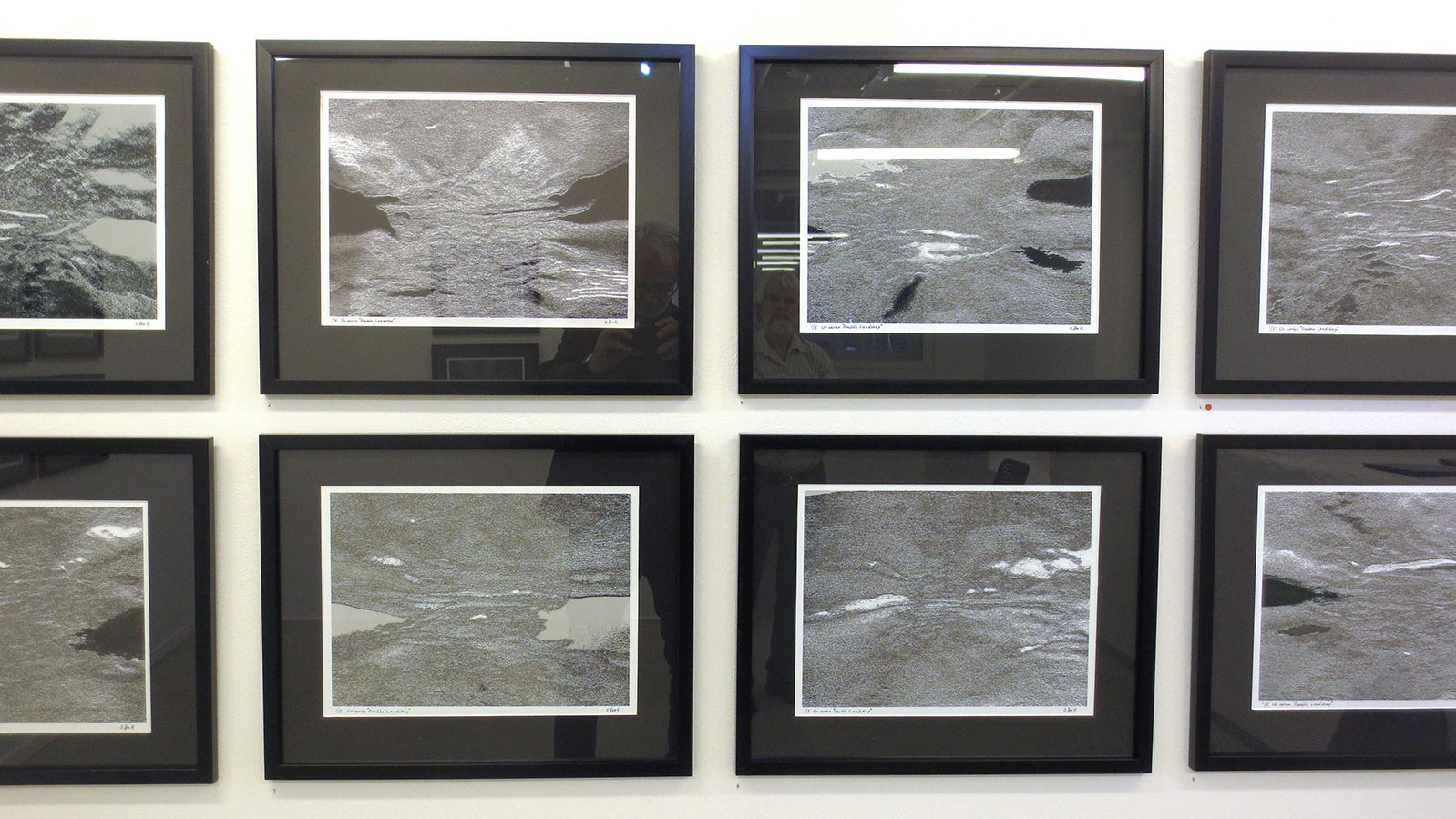 En serie svartvita bilder i svarta ramar i två rader på en vit vägg. 