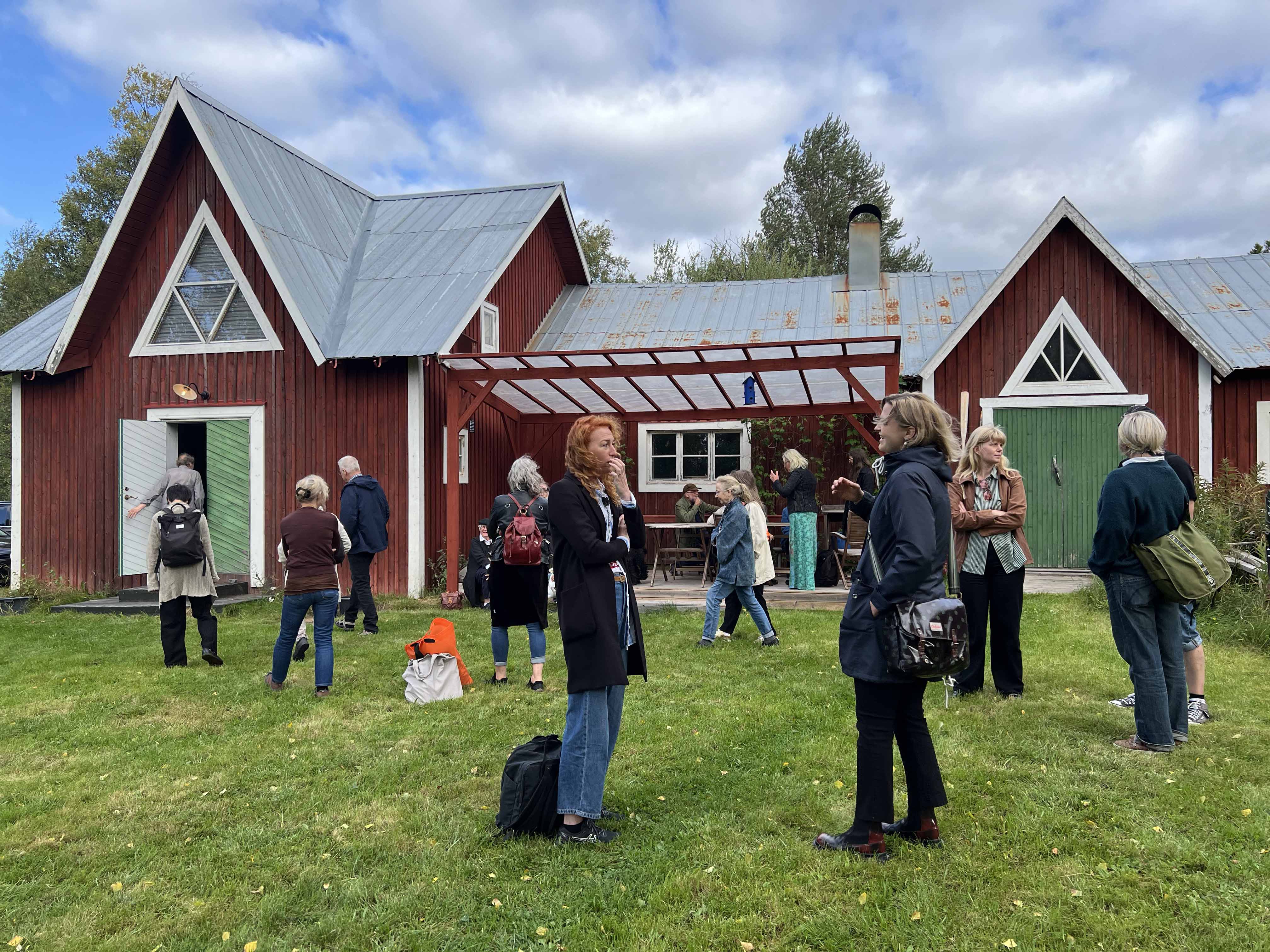 Människor som står på en gräsmatta framför en röd träbyggnad (konsthallen Kvarken)