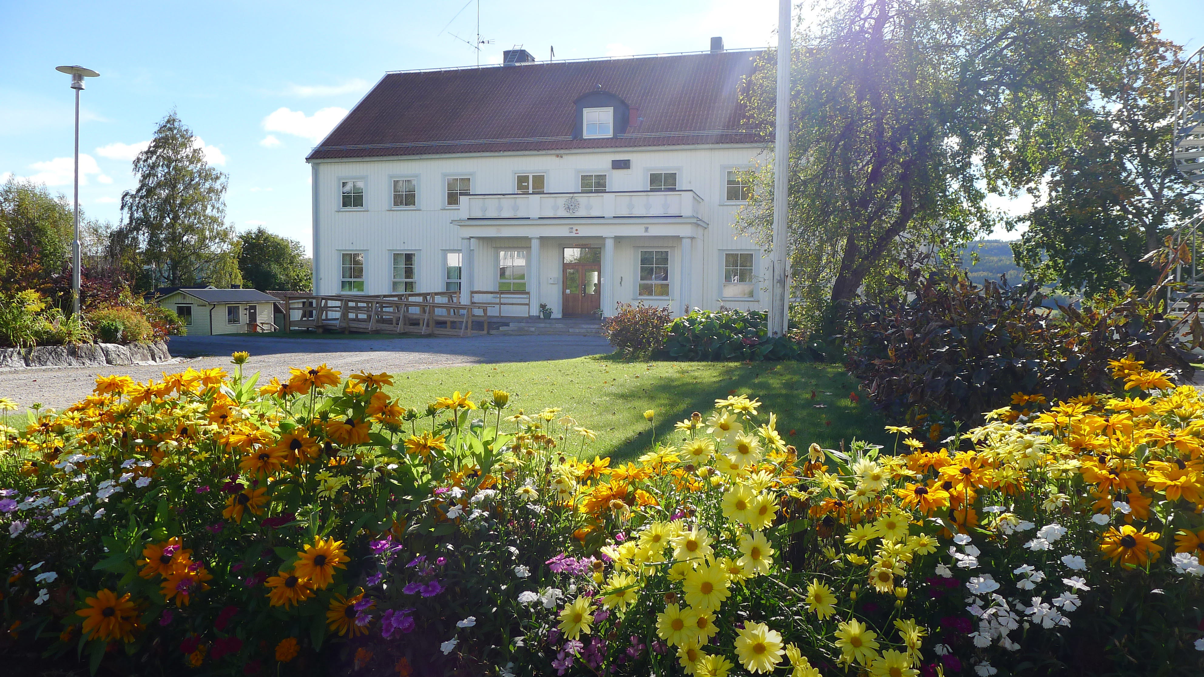 Foto av skolhuset med blommor i förgrunden. 