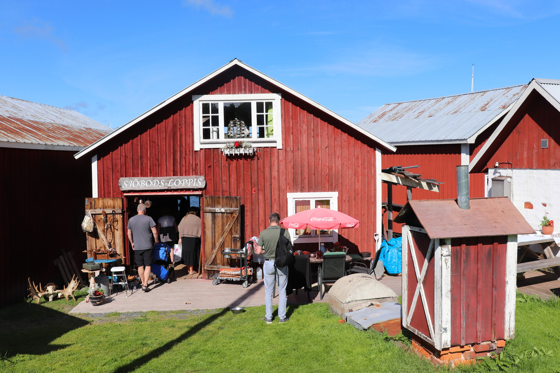 Foto från turiststråk i Bönhamn, Höga Kusten. En röd träbyggnad med flanerande människor utanför. 