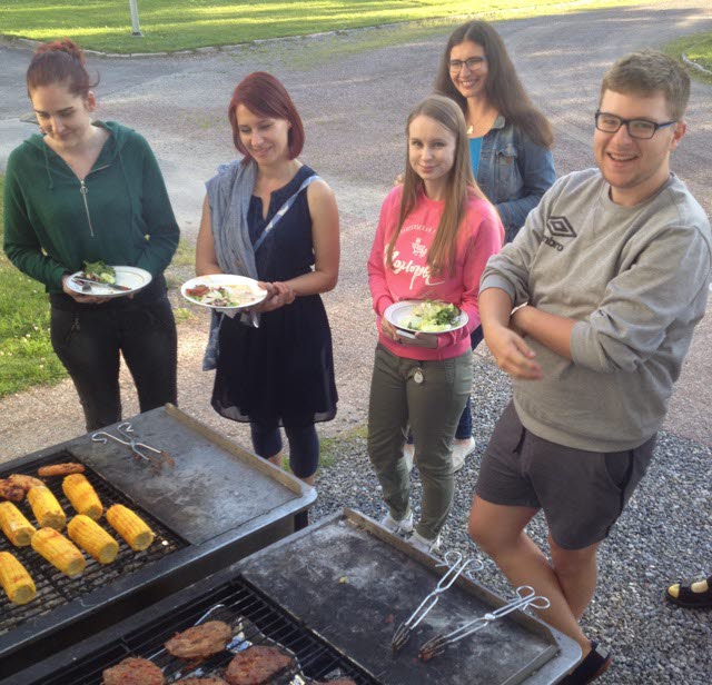 En grupp deltagare står vid en grill med tallrikar med mat.