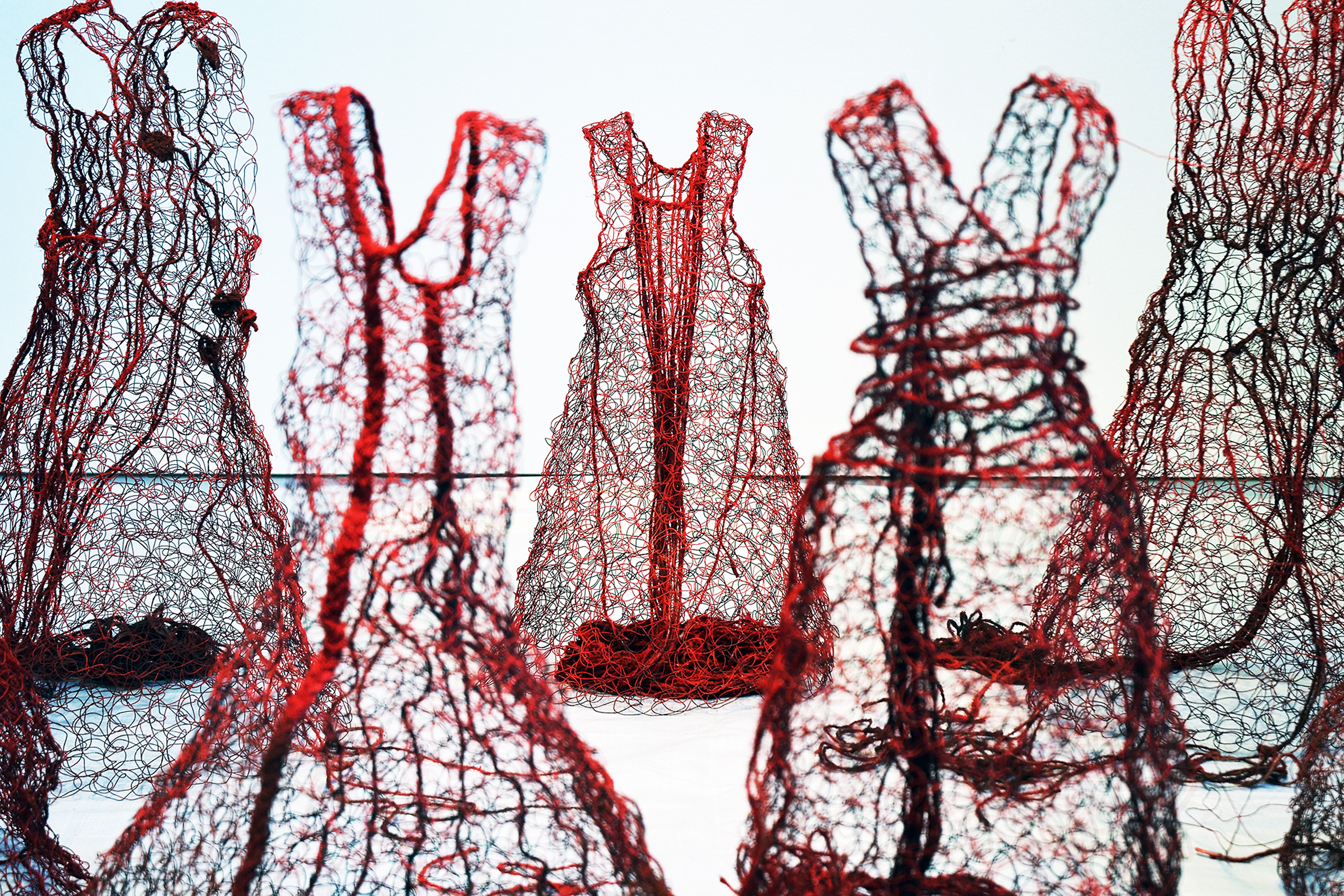 Skulpturer som röda klänningar gjorda i nätliknande textilt material.