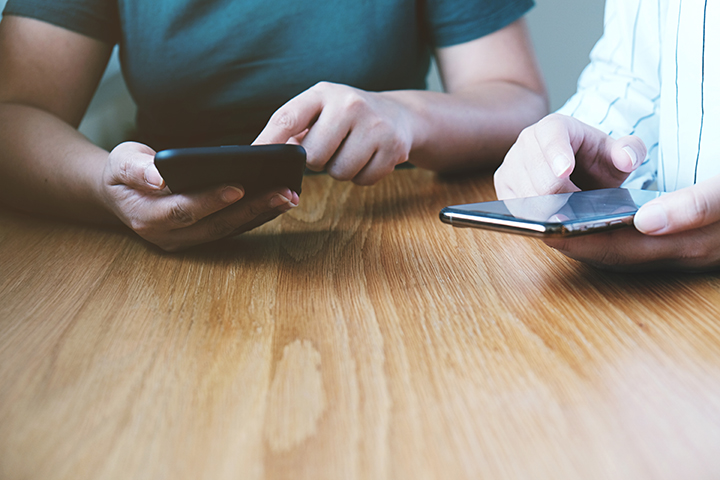 Två personer sitter vid ett bord och håller i varsin mobiltelefon.